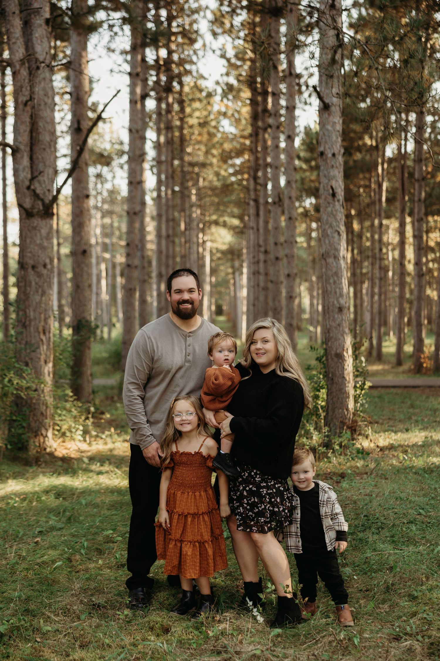 A warm family moment captured between three people in a pine forest at sunset.