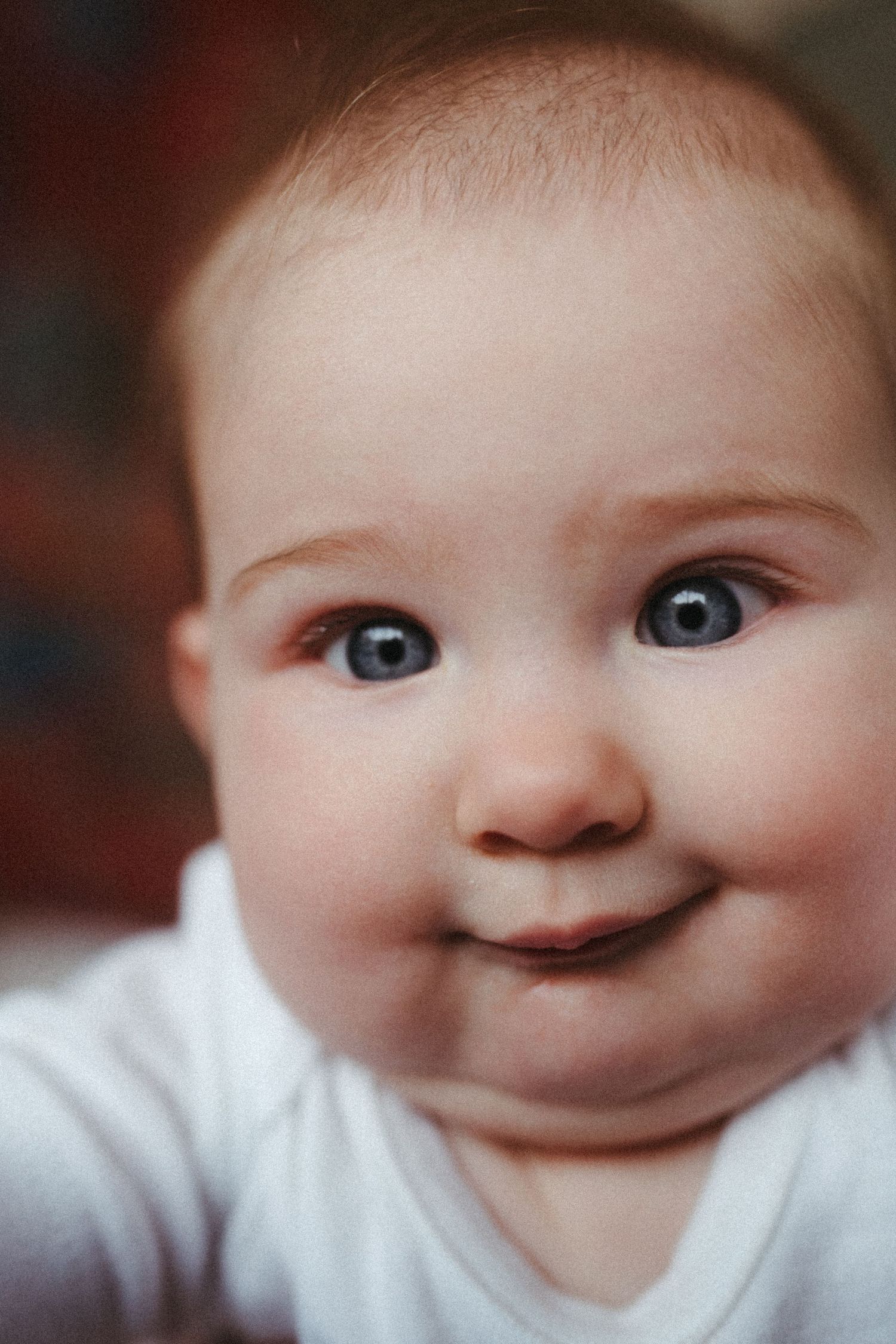 Close-up portrait of baby smiling with bright eyes in white clothing.