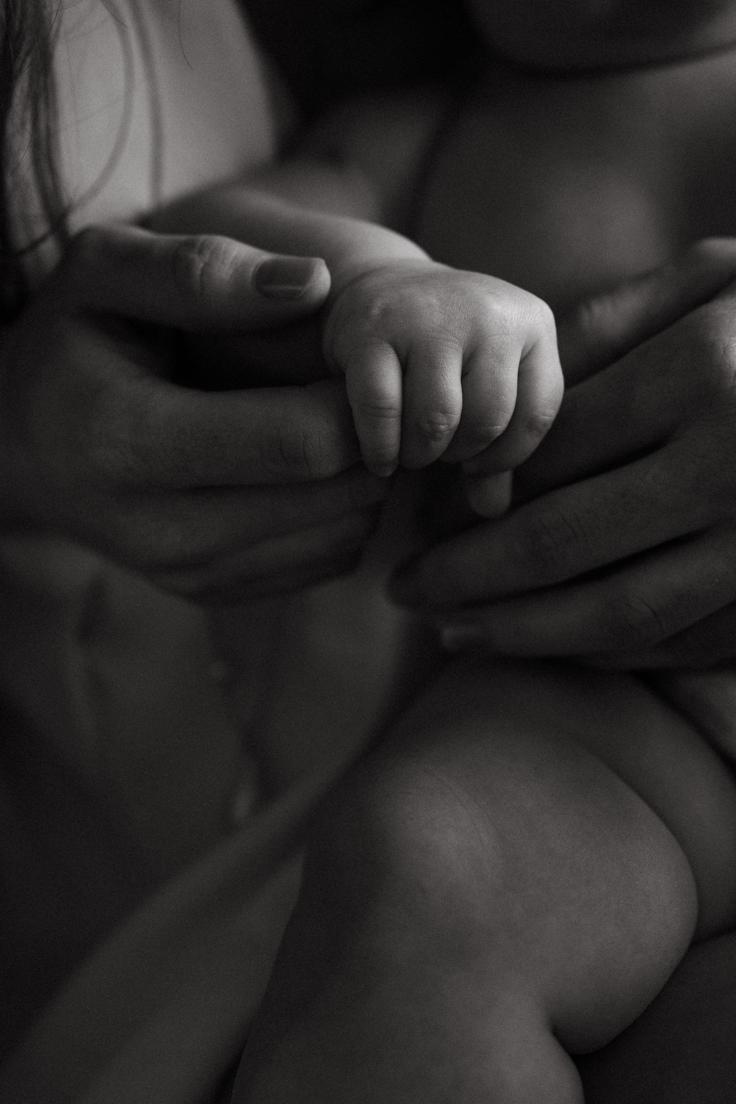 Intimate black and white photograph capturing soft details of infant skin and hands.