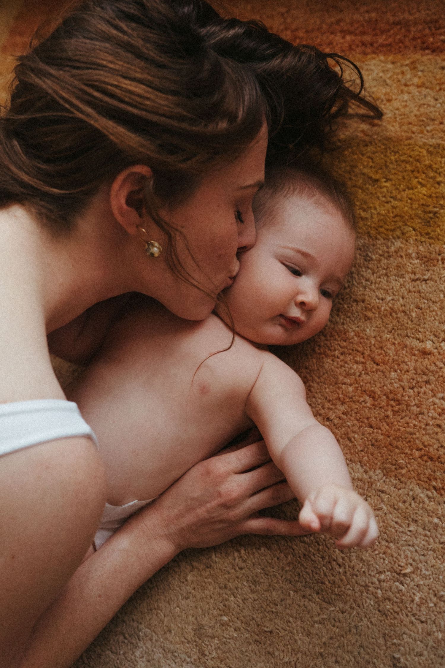 An intimate moment between a mother and baby in warm tones as they lie together.