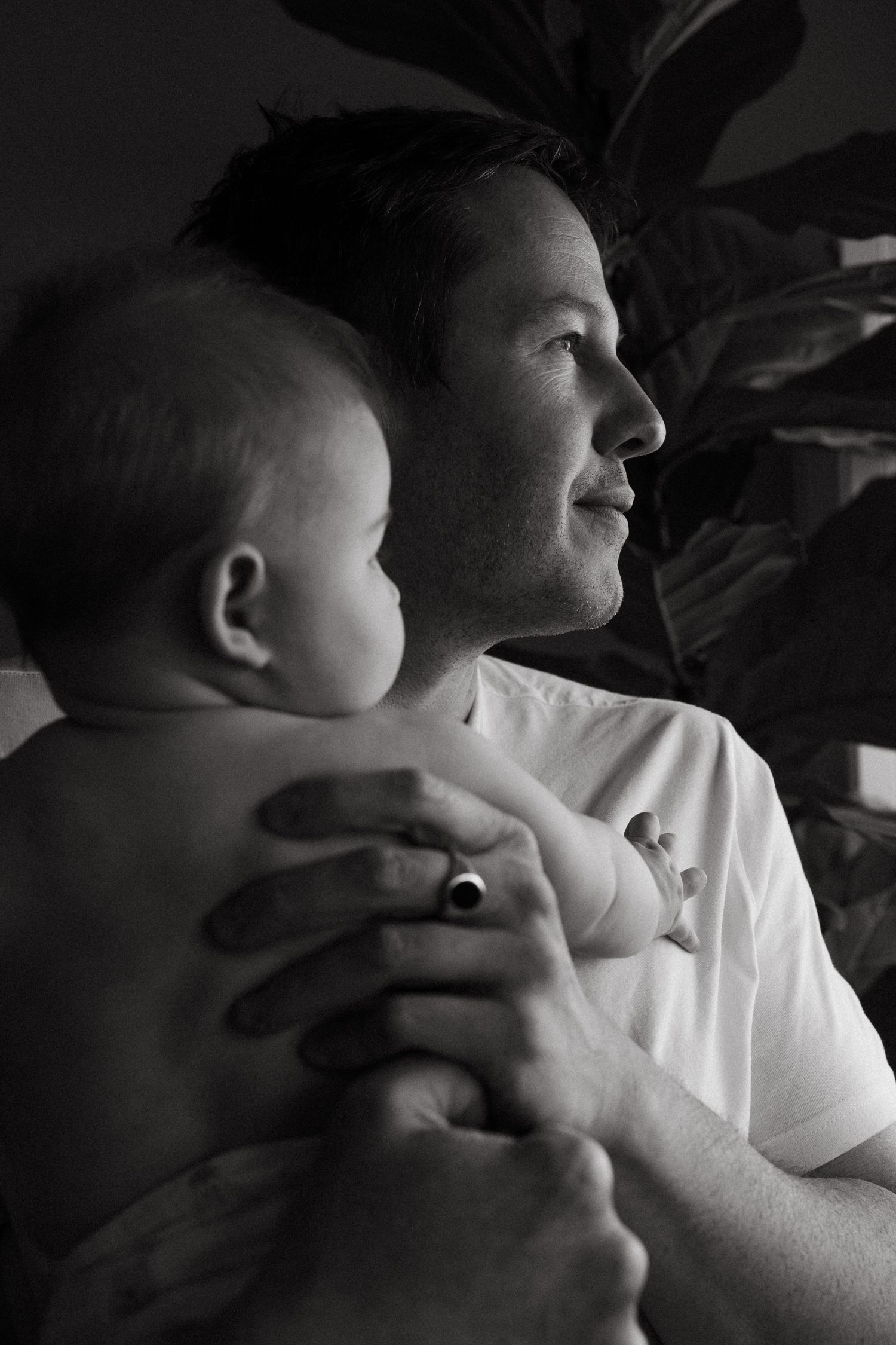 A black and white portrait of a parent holding their baby while looking off to the side.
