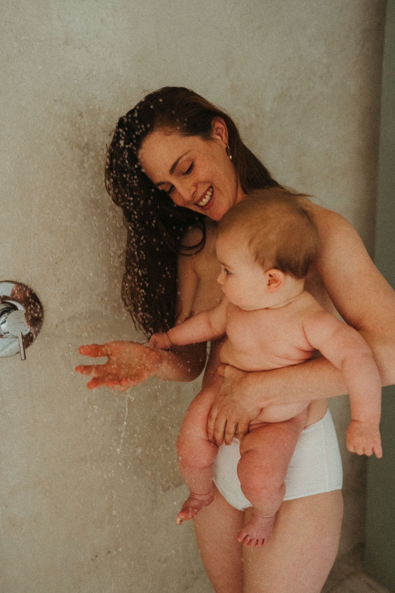 A joyful mother with wet hair holds her smiling baby during bathtime.