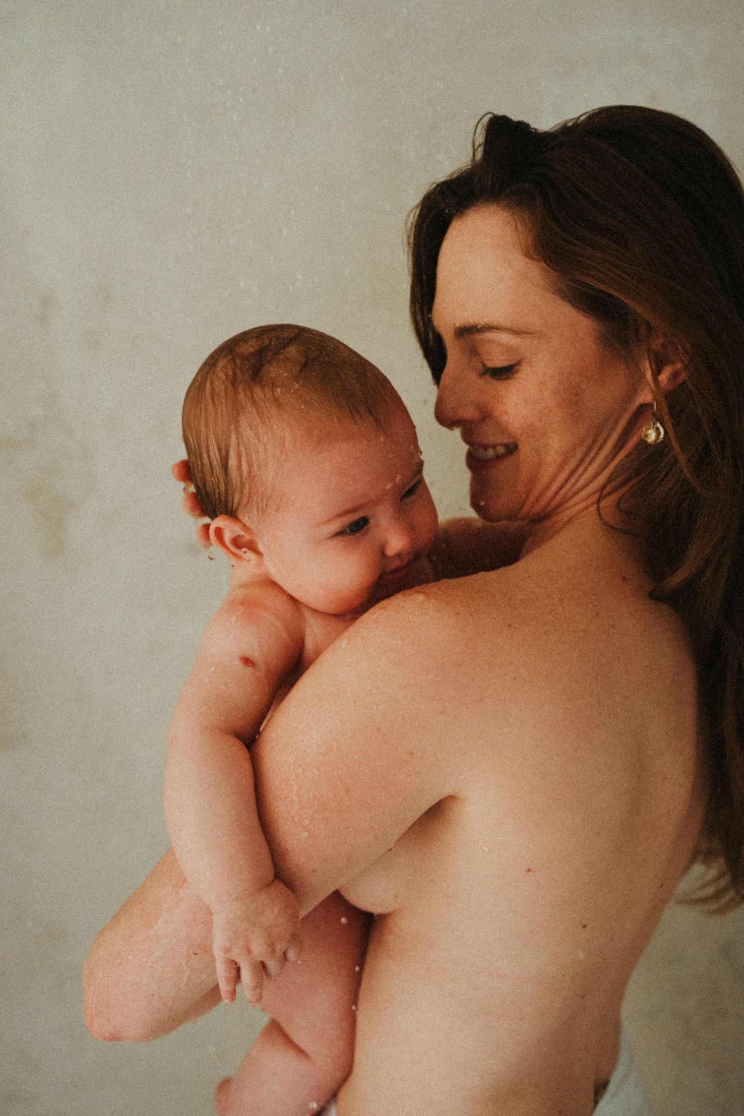 An intimate portrait of a mother holding her naked baby against her bare shoulder.
