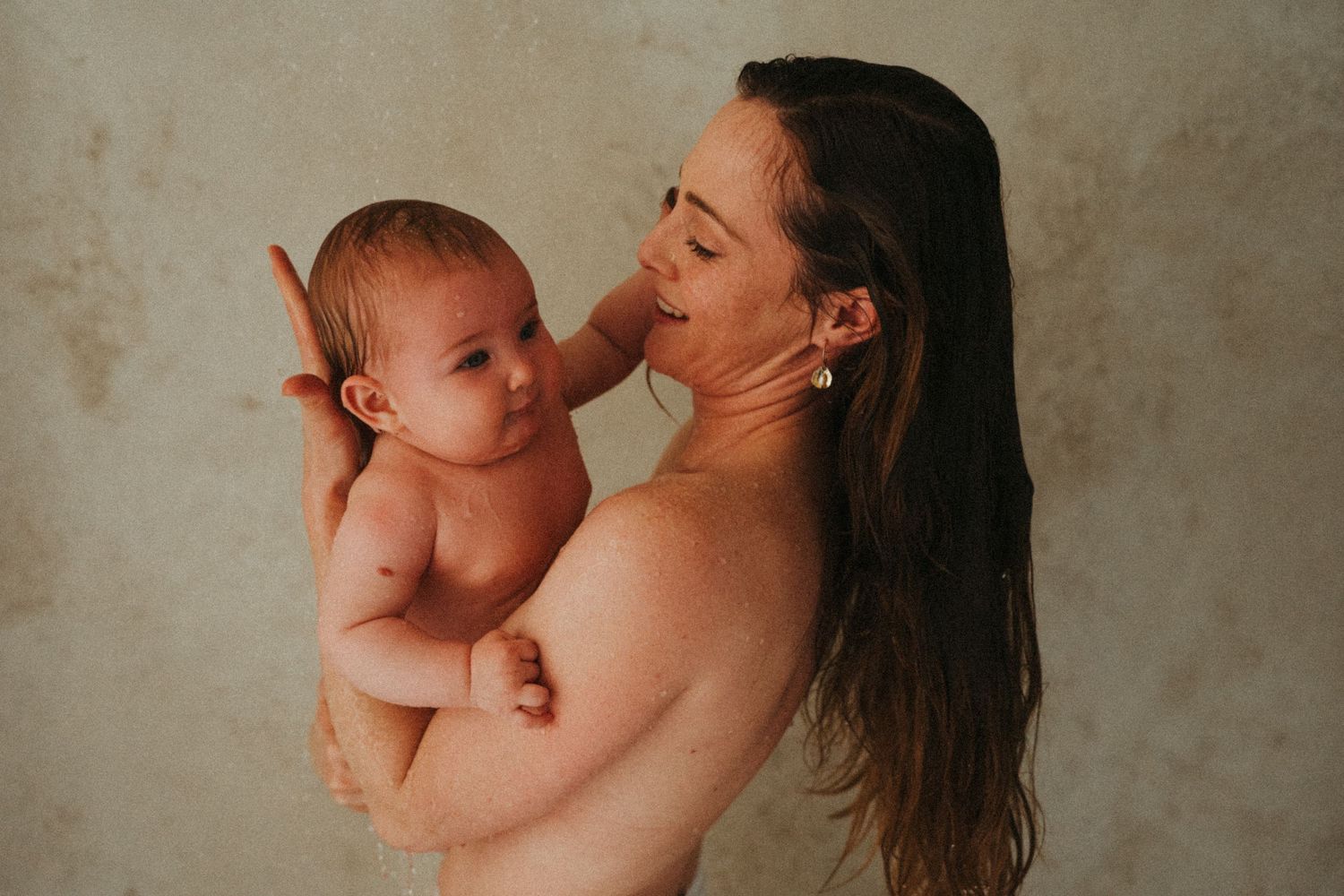 A tender moment between mother and baby in warm lighting against a neutral background.