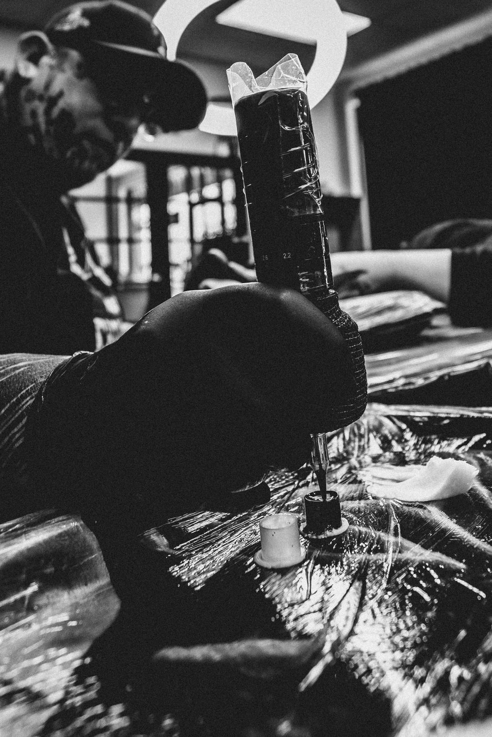 Black and white close-up of a tattoo artist working with a tattoo machine on a client at a tattoo studio.