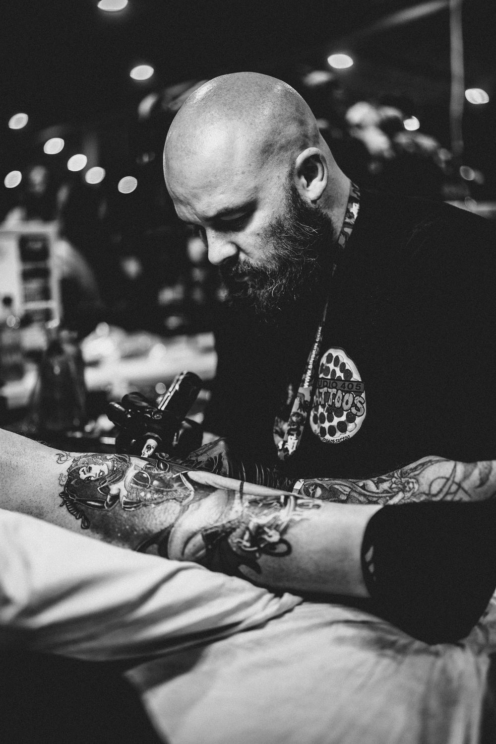 Black and white photo of a tattoo artist focused on creating a detailed tattoo in a studio setting.