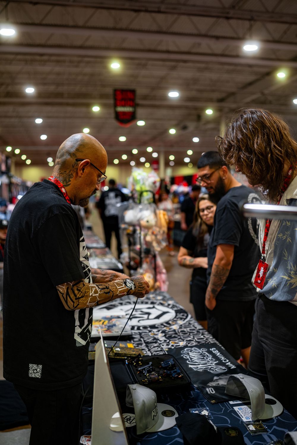 Vendors and attendees gather at a merchandise table during an indoor convention or event.