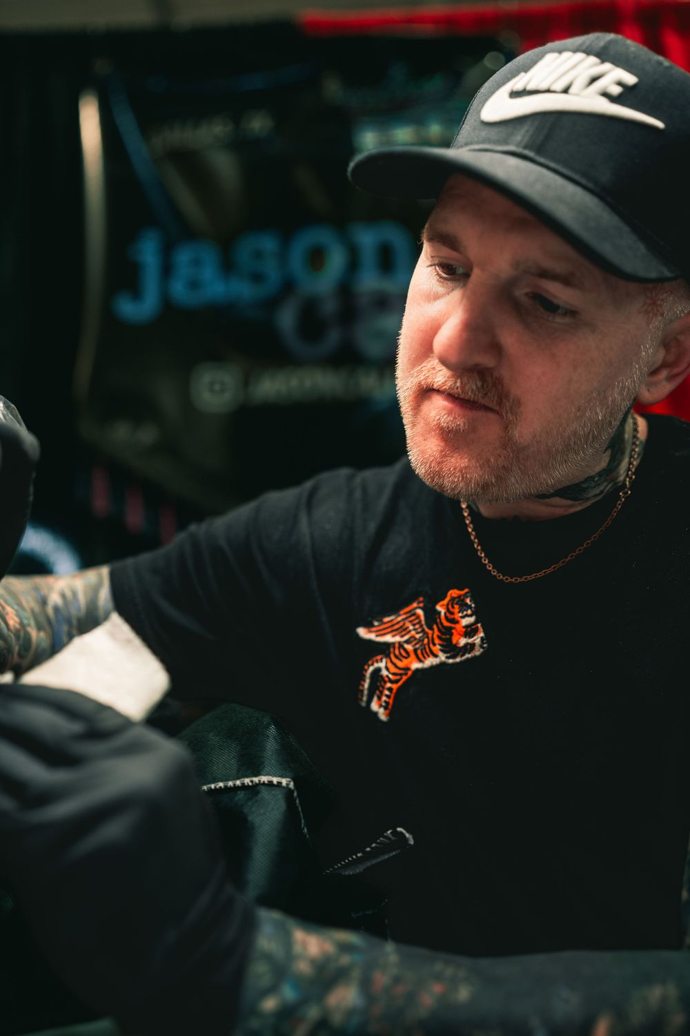 Person wearing a black Nike cap and dark shirt with orange graphic design sits indoors in dim lighting.