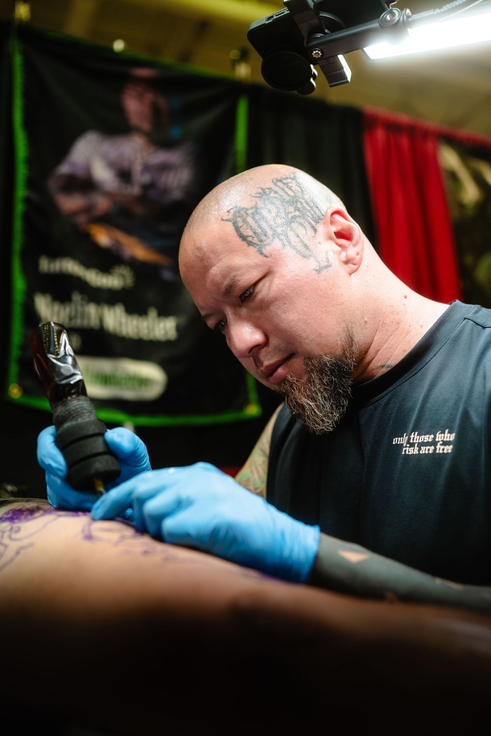 A focused tattoo artist wearing blue gloves works carefully with a tattoo machine in a professional studio setting.