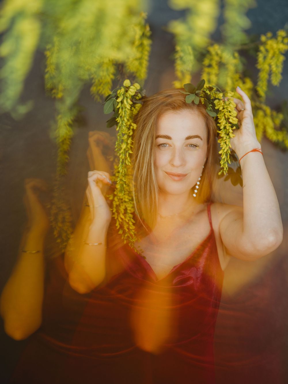 A person poses beneath yellow spring blossoms against a dark background in a creative portrait series.