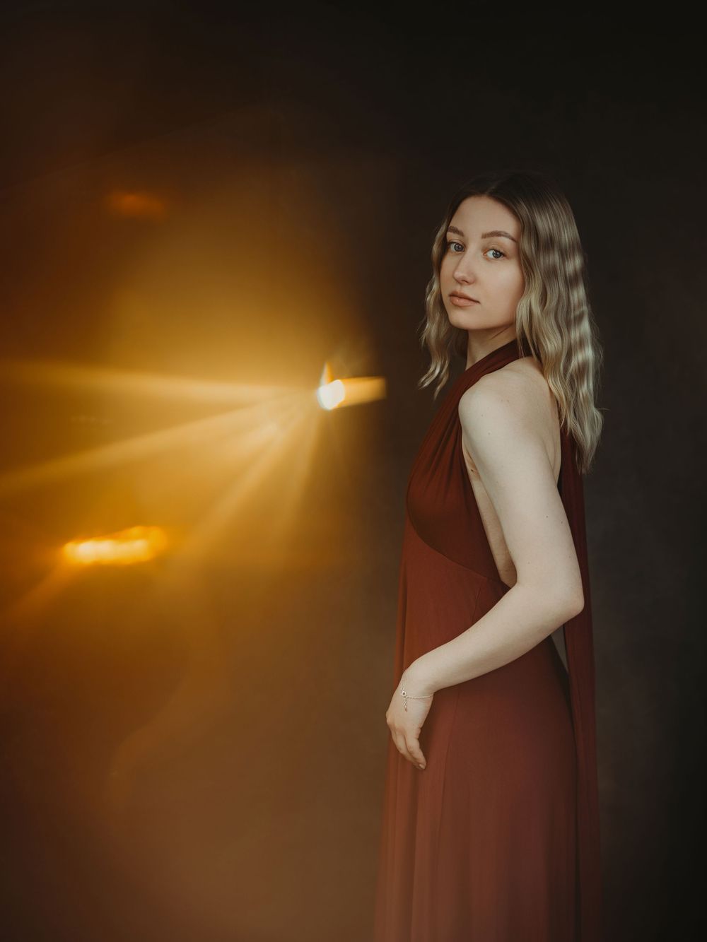 A series of moody portraits in burgundy dress against dark background with dramatic golden sunlight flares.