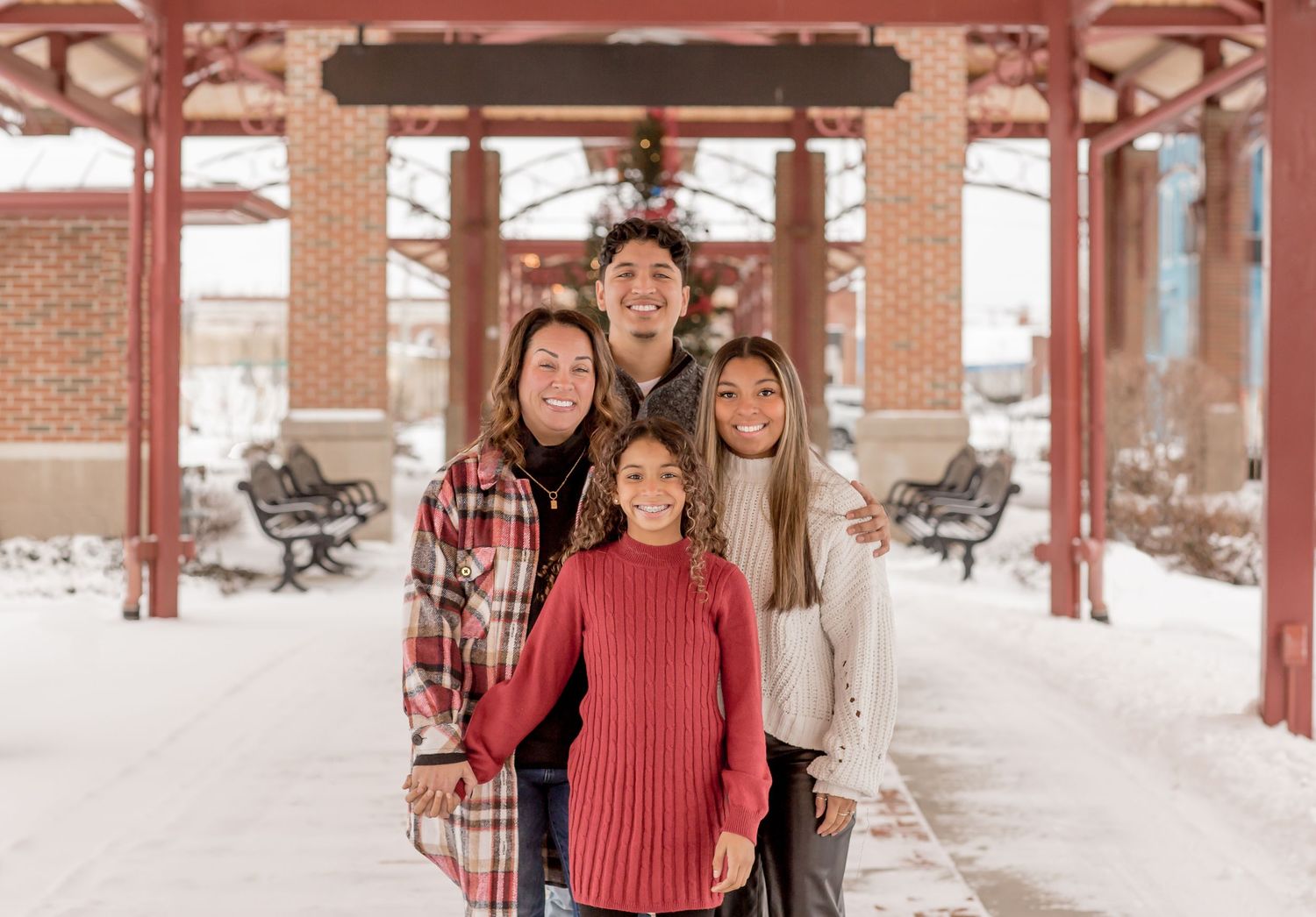 Family of four smiling together under snowy brick pavilion in winter.
