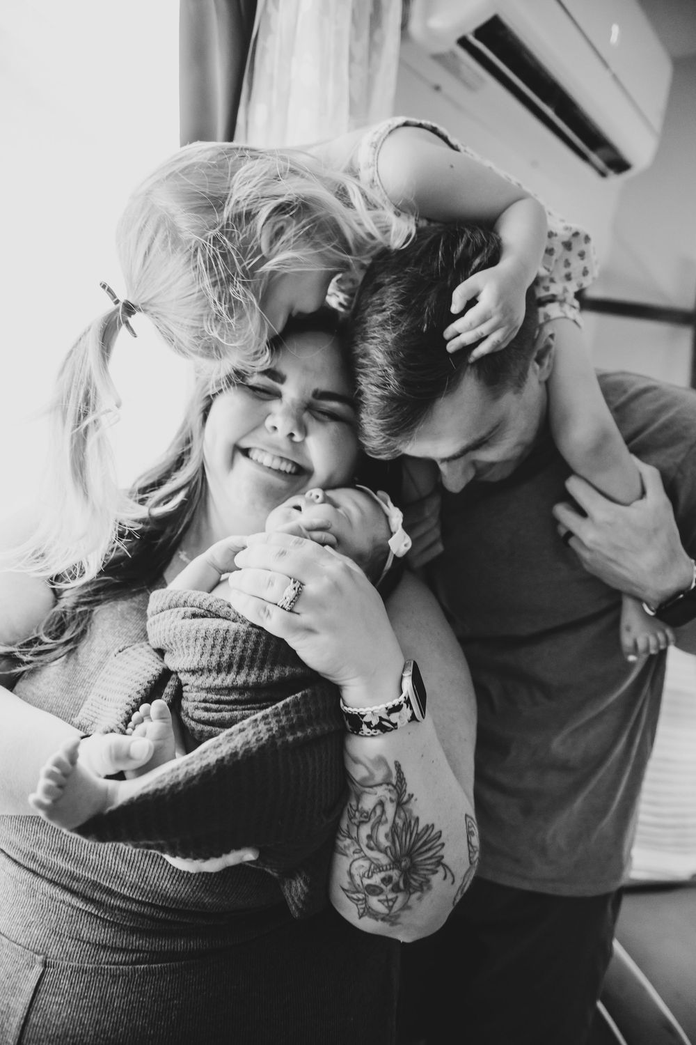Black and white photo of family cuddling with newborn baby.