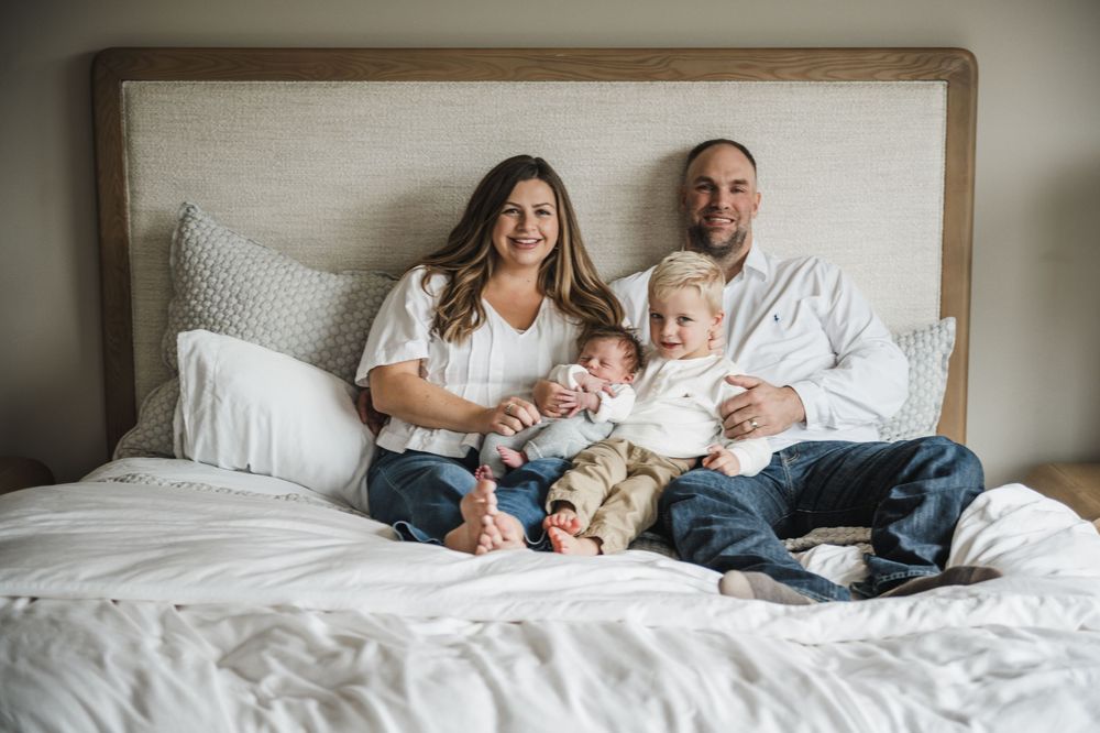 Family lying together on a white bed in a cozy bedroom during an intimate lifestyle photo session.