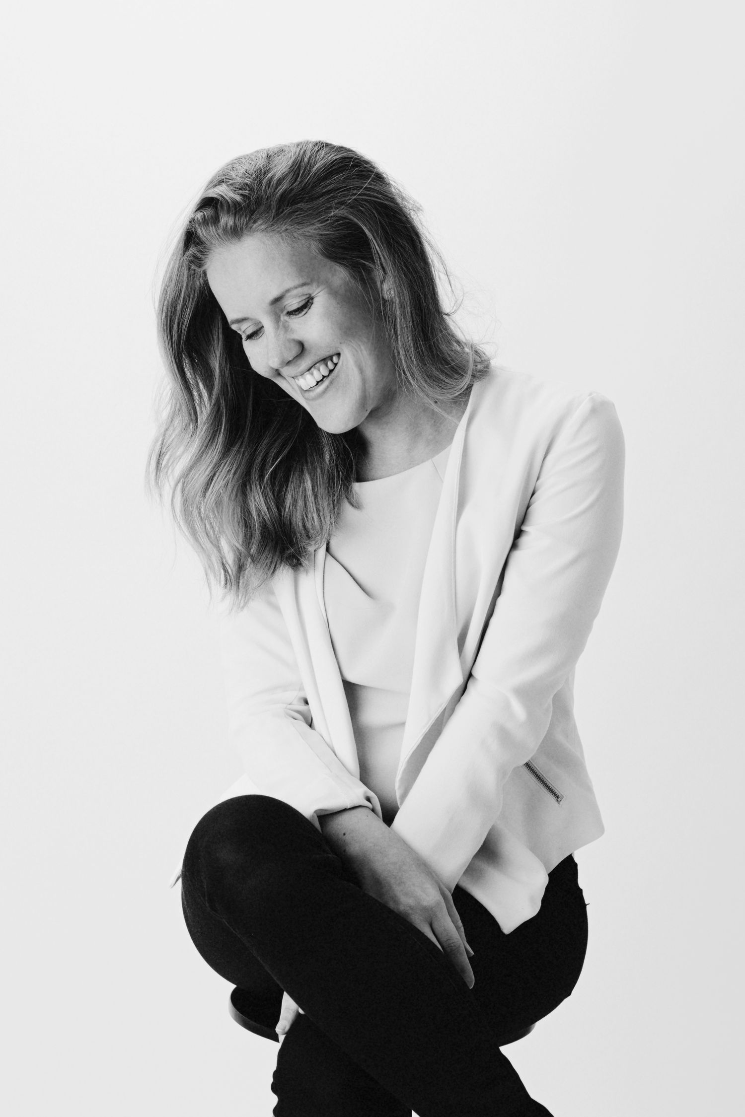 Black and white portrait of someone with wavy hair laughing while wearing a white blazer and dark pants.