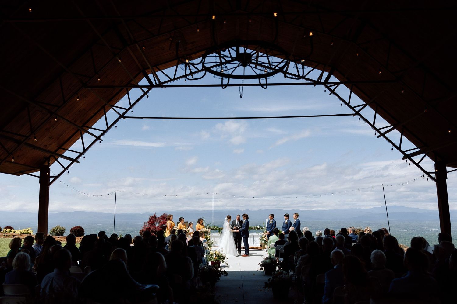 An outdoor wedding ceremony set against mountains with white chairs and rustic wine barrels.