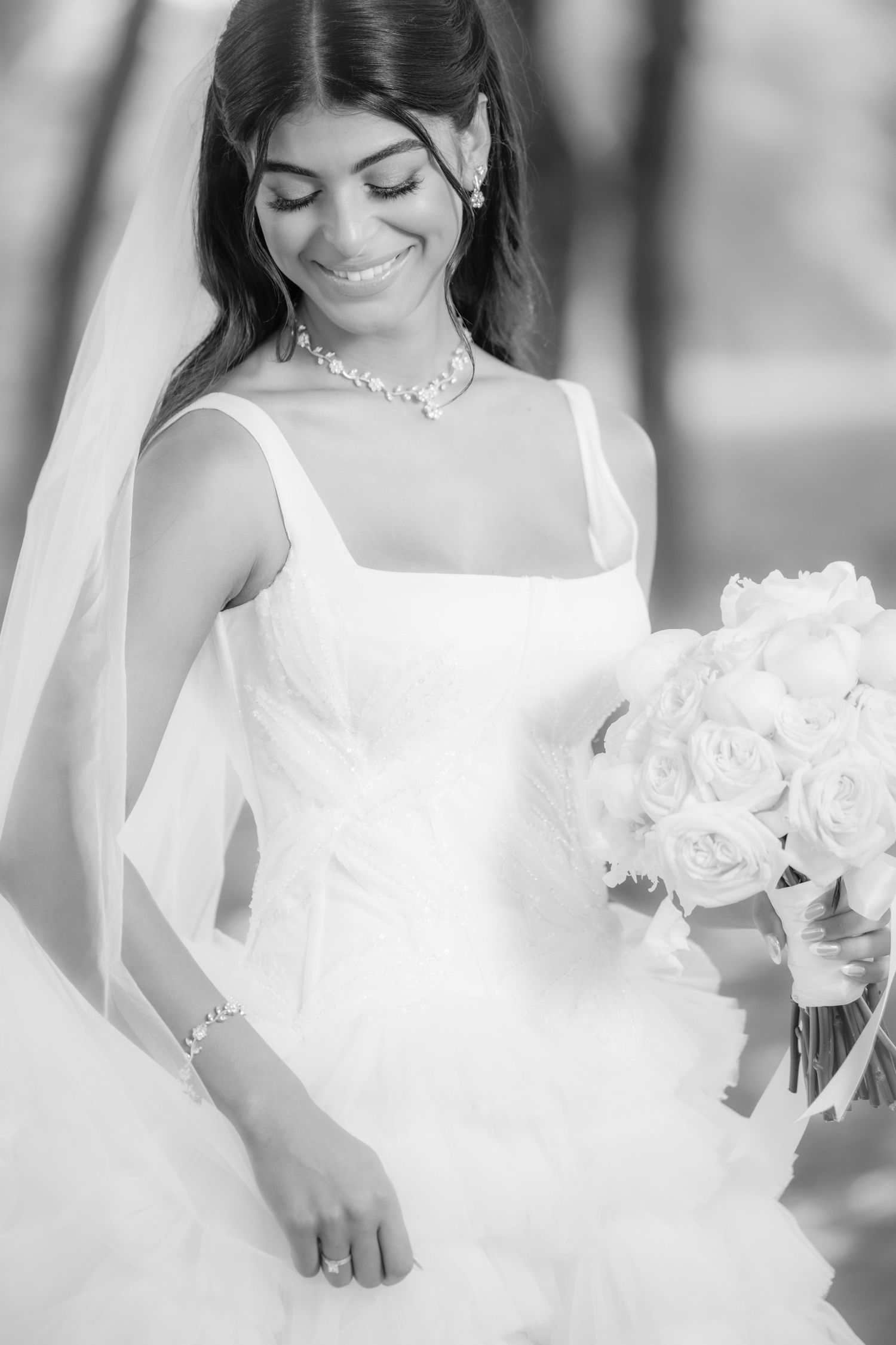 A gentle black and white portrait of a radiant bride in a white gown holding a bouquet of roses on her wedding day.