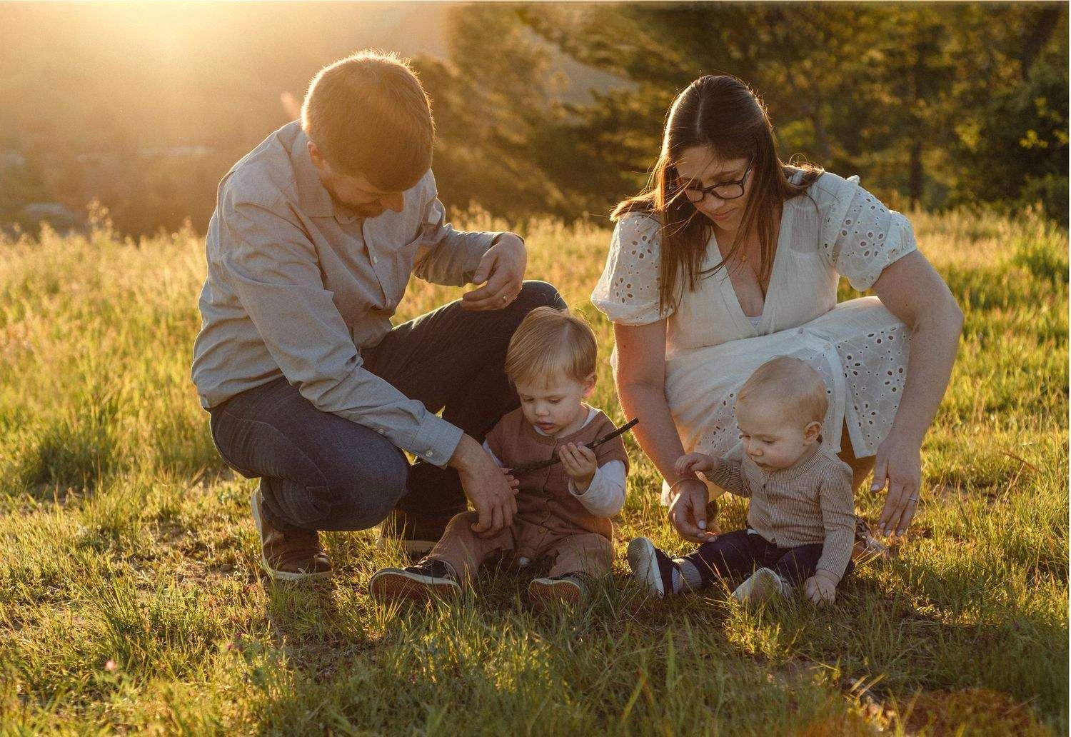 Family sitting together in a sunlit meadow during golden hour playing with toys.
