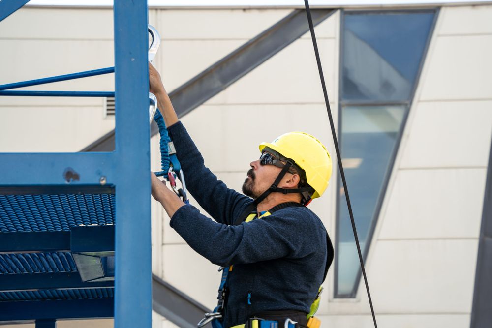 Worker in safety gear and yellow hard hat installing equipment on a blue metal structure.