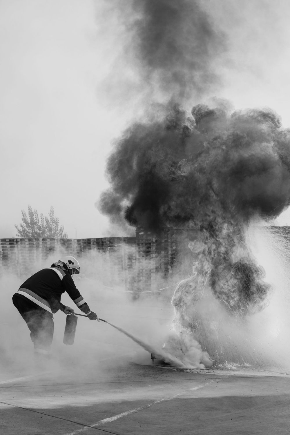 Firefighter controlling a large smoke plume with water spray in black and white.
