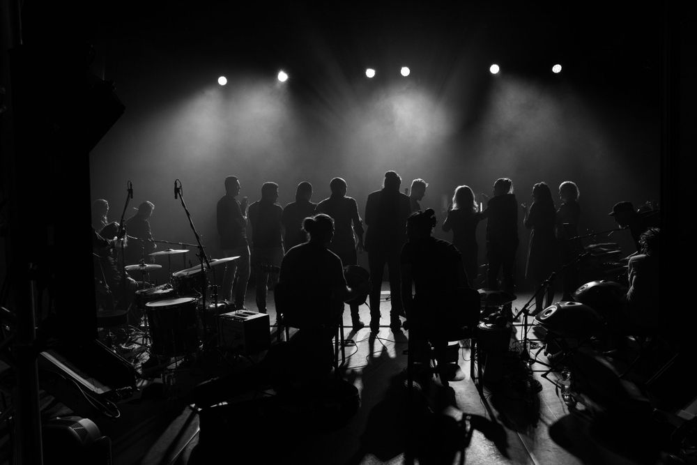Silhouettes of performers on stage with dramatic backlighting creating a moody atmosphere.