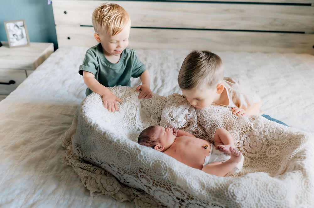 Children laying together on white bedding in a casual lifestyle photography session.