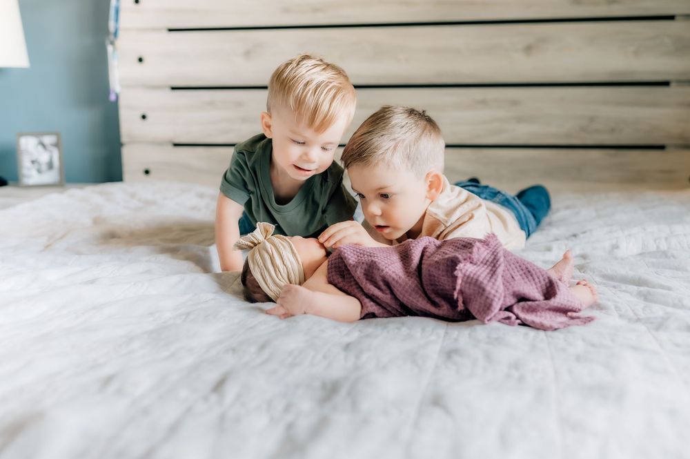 Two children play and laugh together on a soft white bed.