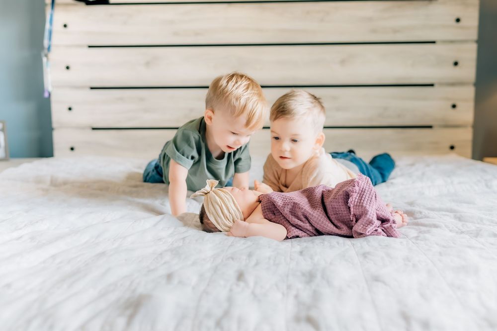 Two young children lying together on white bedding looking at each other.