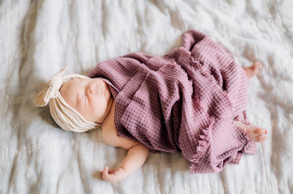 Sleeping infant wrapped in a soft mauve waffle-textured blanket lying on white bedding.