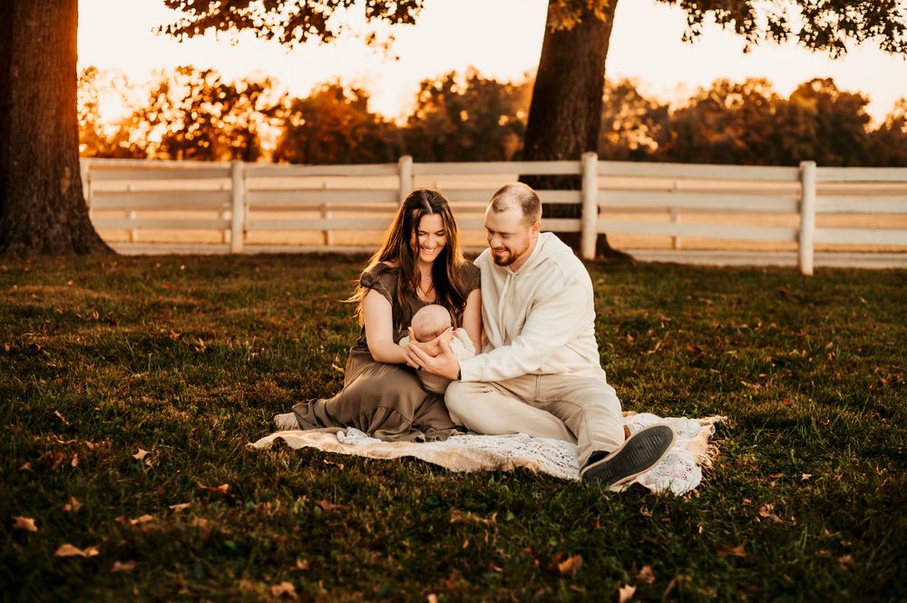 A couple sitting on blanket with baby during golden hour near white fence.