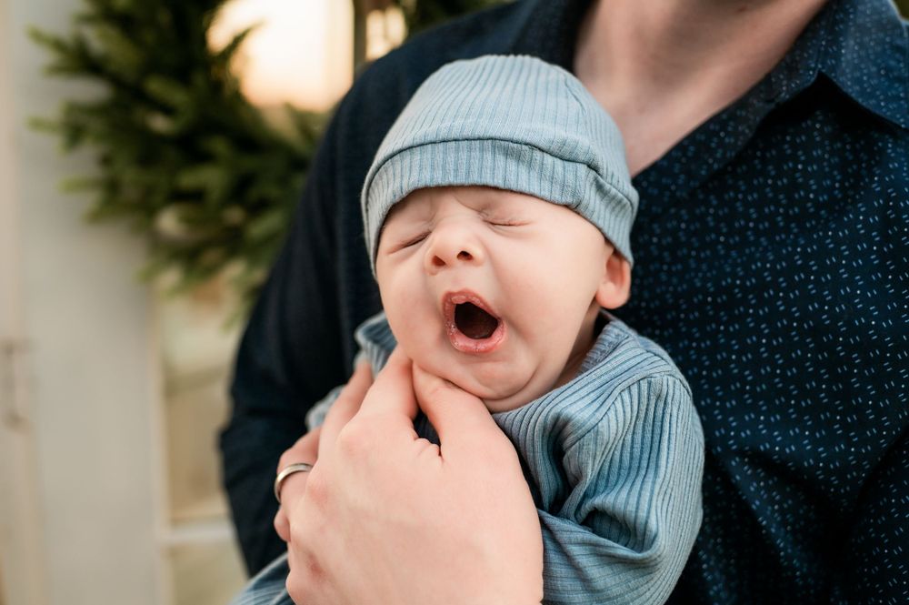 Close up of a yawning baby wearing a light blue knit hat and sweater.