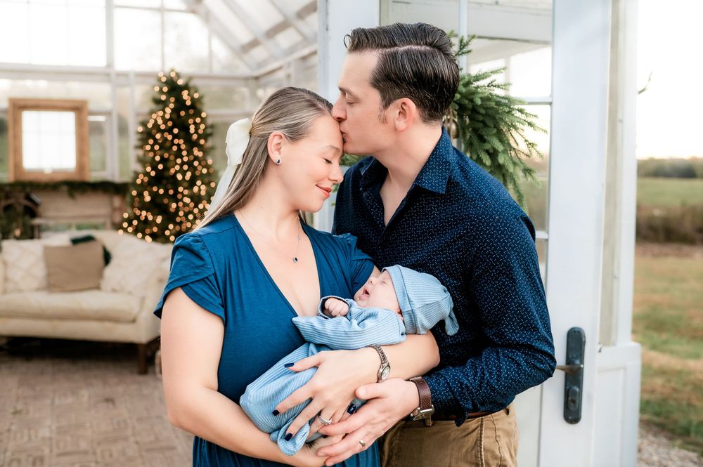 A sweet family moment captured outdoors with a baby in blue against a rustic backdrop.