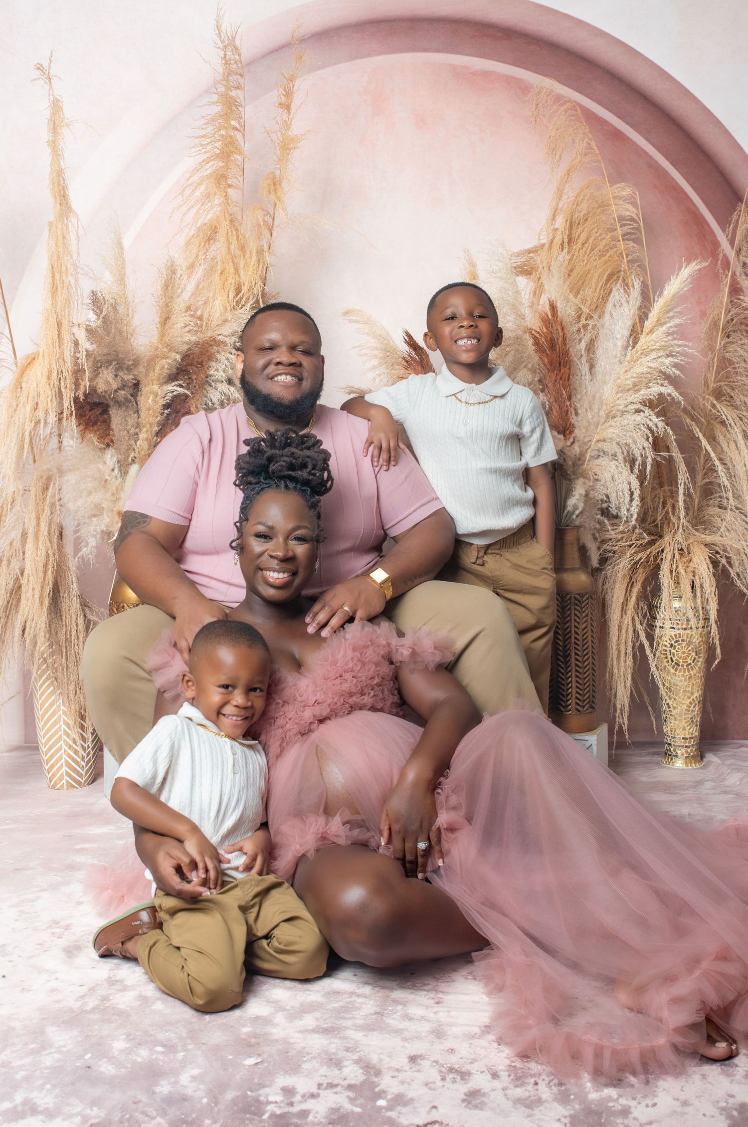 A happy family poses together on the floor with pampas grass decorations and pink tulle fabric in a studio setting.