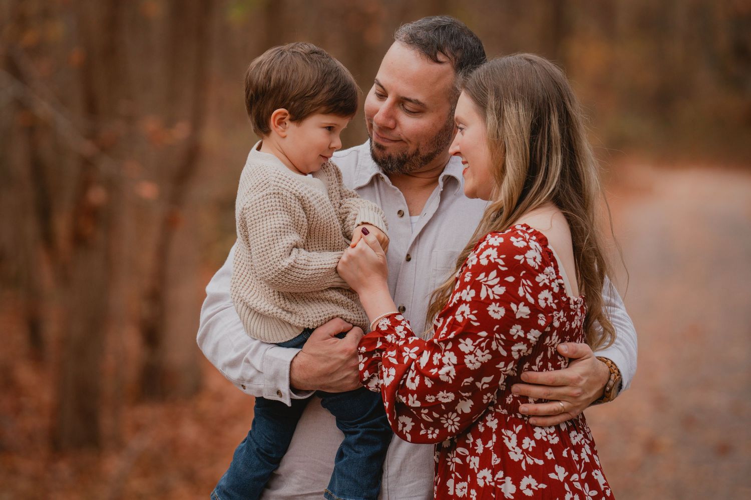 Parents holding young toddler in a tender embrace on an autumn forest path.