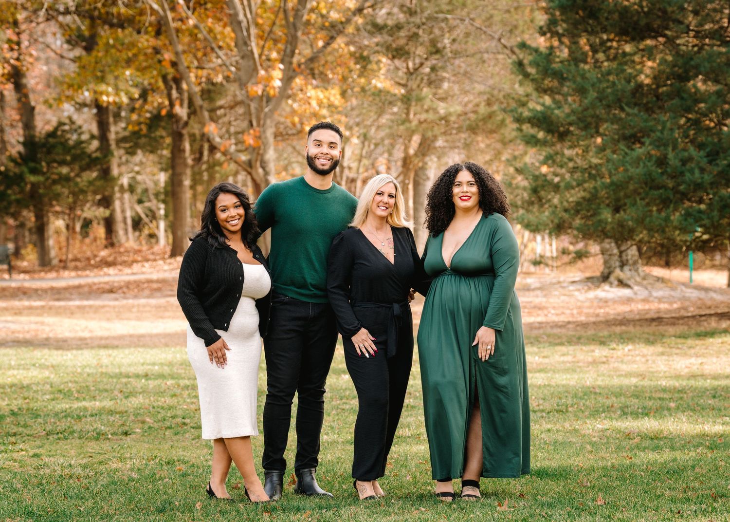 Group of four adults posing outdoors in elegant black and green outfits in a park setting.
