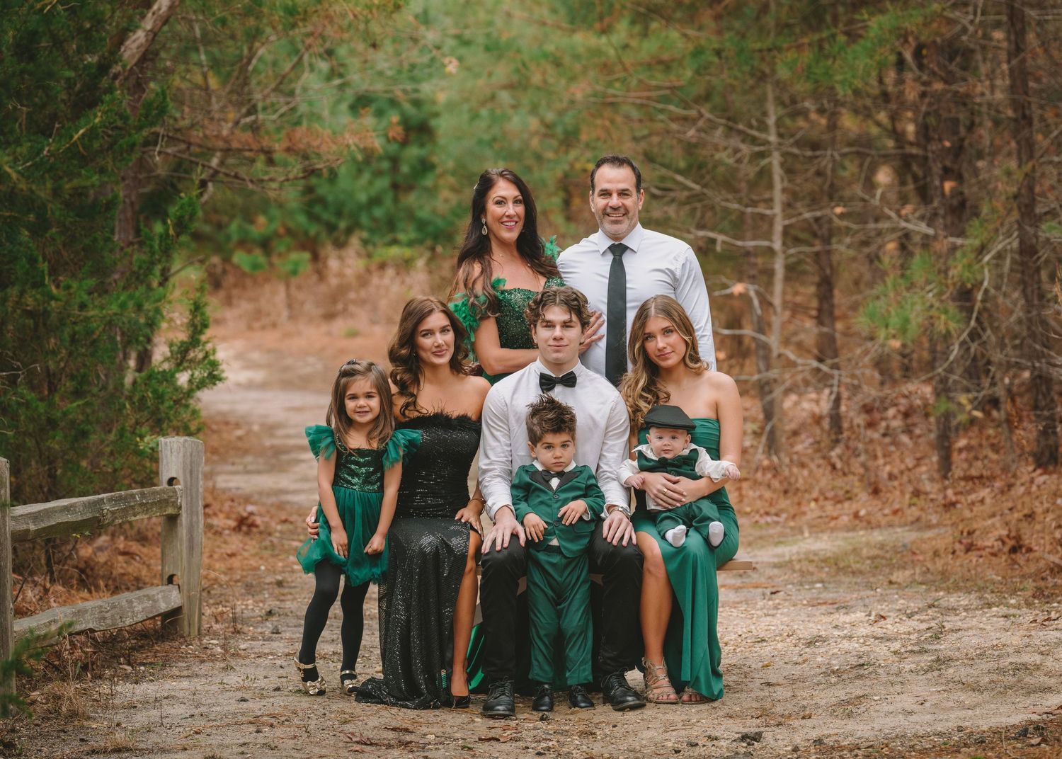 Large family portrait in matching green outfits on a wooded dirt path in autumn.