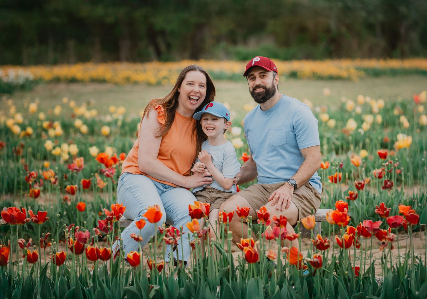 Family of three sitting in a vibrant tulip field with red and yellow flowers in bloom.