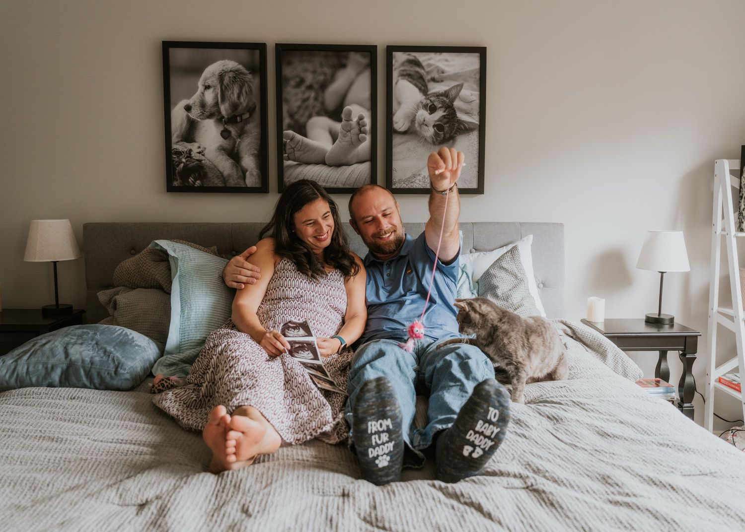 Couple sitting on a bed smiling and holding an ultrasound photo announcing their pregnancy.