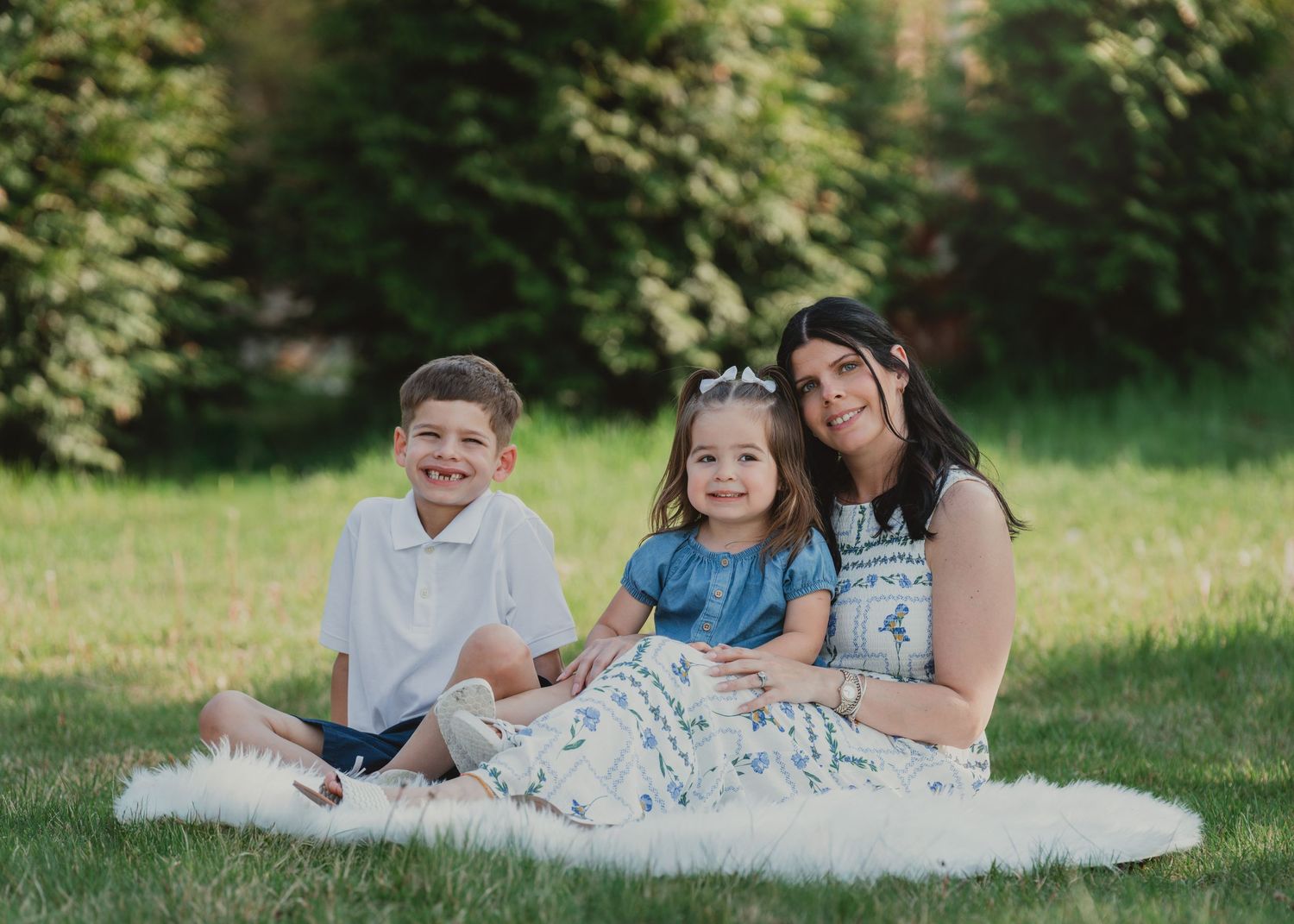 Mother sitting on grass with two young children during an outdoor family portrait session.