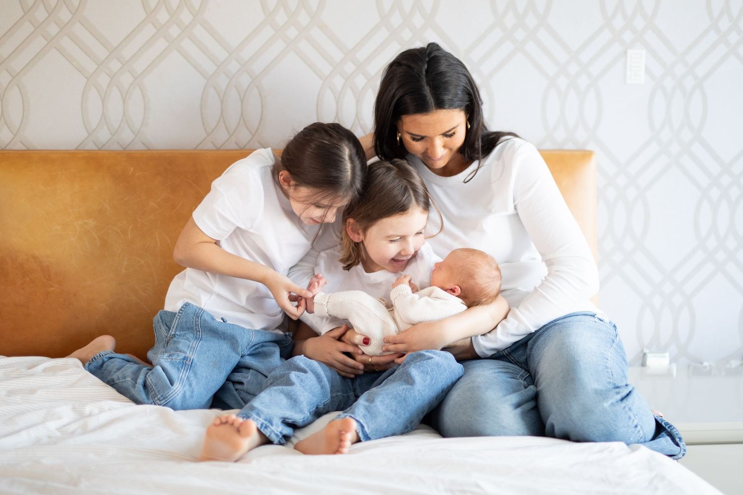 Family in casual denim sits together on couch while reading and bonding with newborn baby at home.