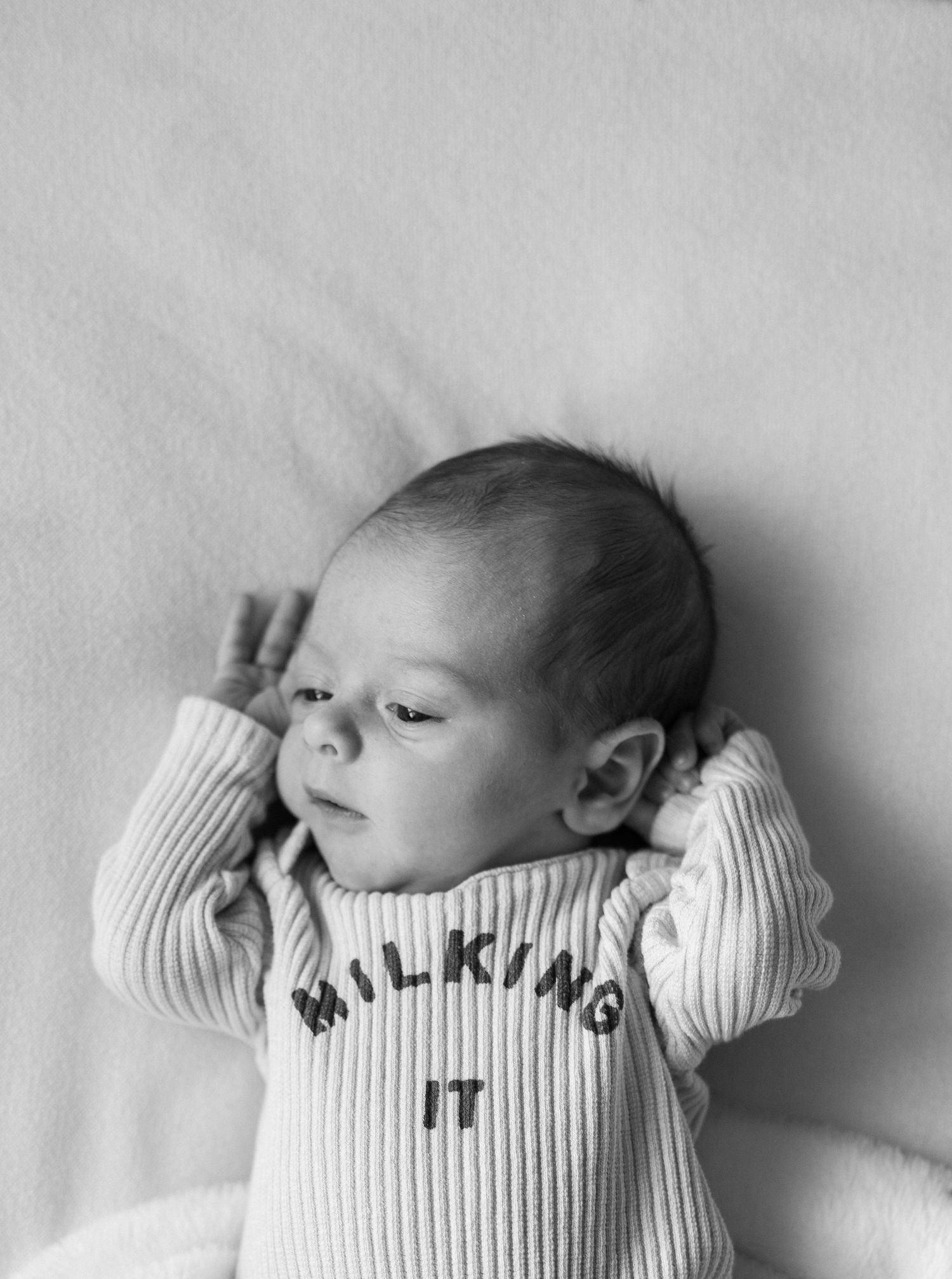 Black and white photo of a newborn baby wearing a ribbed romper that reads Milking It, lying on a soft blanket.