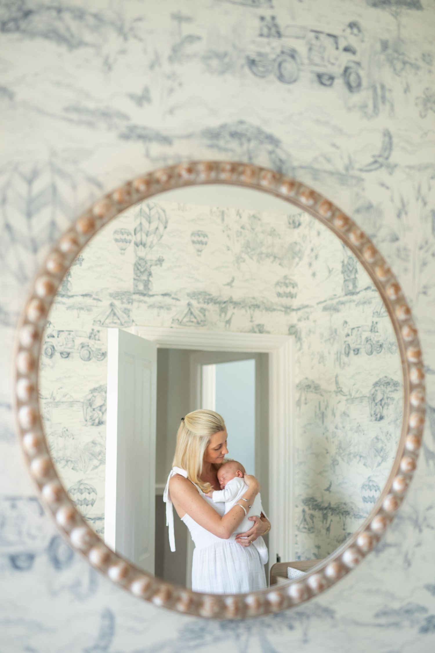 A series of oval mirrors with decorative frames mounted on a light blue toile wallpapered wall.