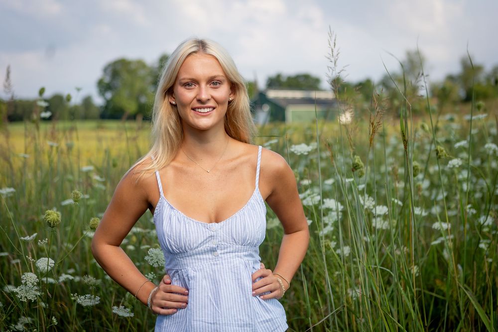 Woman in blue sundress poses in a blooming wildflower meadow on a sunny summer day.