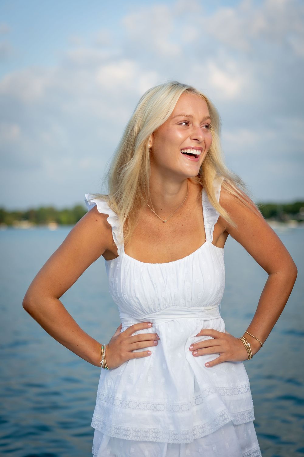 A series of joyful portraits in a white sundress against a waterfront background with blue sky and clouds.