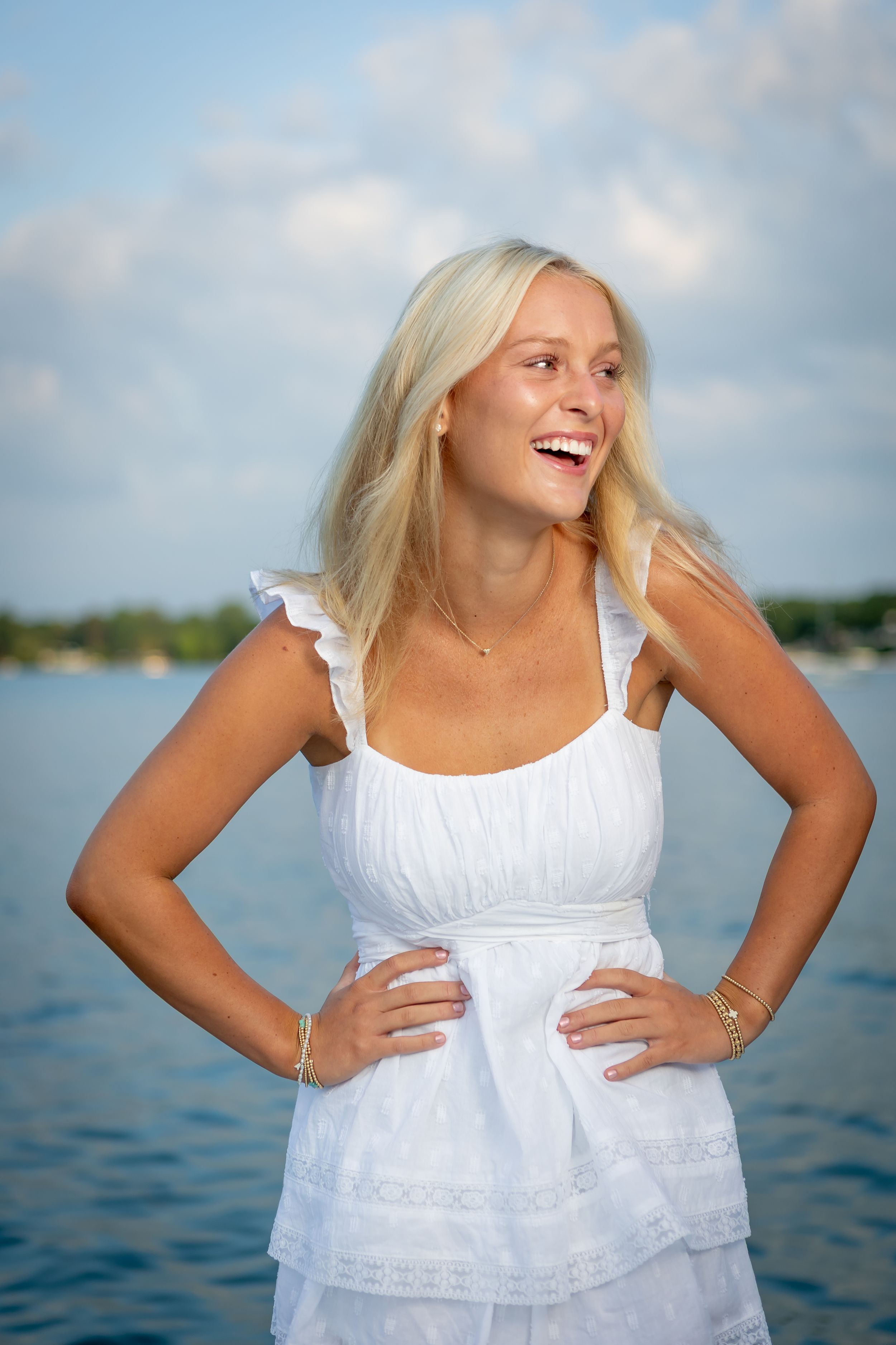 A series of joyful portraits in a white sundress against a waterfront background with blue sky and clouds.