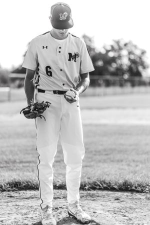 Black and white baseball player in uniform number 6 stands on field holding glove in contemplative pose.