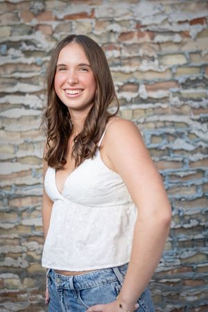 Portrait series against rustic brick wall showing casual summer style with white top and denim in natural lighting.