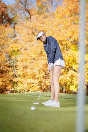 Golfer lines up a putt on a green golf course surrounded by vibrant fall foliage with golden yellow leaves.