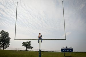 A series of football goal posts stand tall against a cloudy sky on an empty sports field.