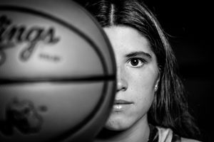 Dramatic black and white portrait of basketball player with ball covering half their face.